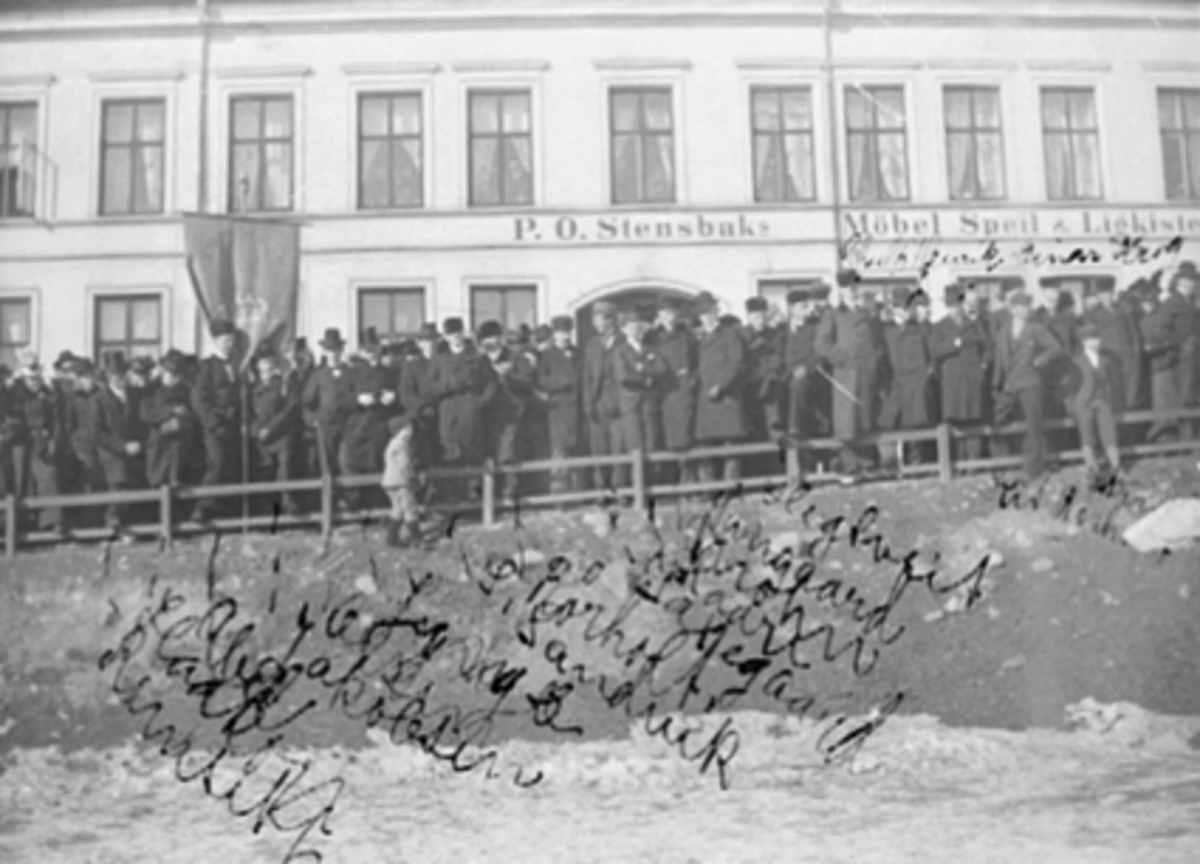 Østre Torg, Hamar by 50 år. Byjubileet 1899. Gruppe menn, fane, opptogforan P.O.Stensbaks møbel, Speil og Likkistefabrikk,