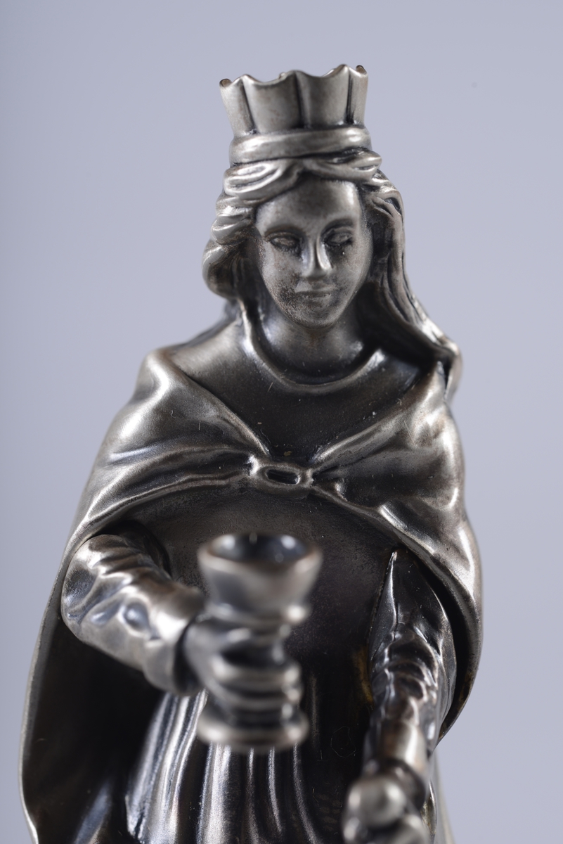 Blankpolert statuett av St. Barbara, skytshelgen for blant annet gruvearbeidere. Hun har en krone på hodet, holder en kopp og et sverd, og står over en steinbygning.