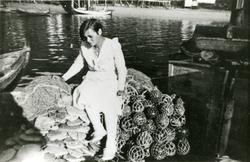 En kvinne sitter på fiskegarn og kavler ombord i en båt