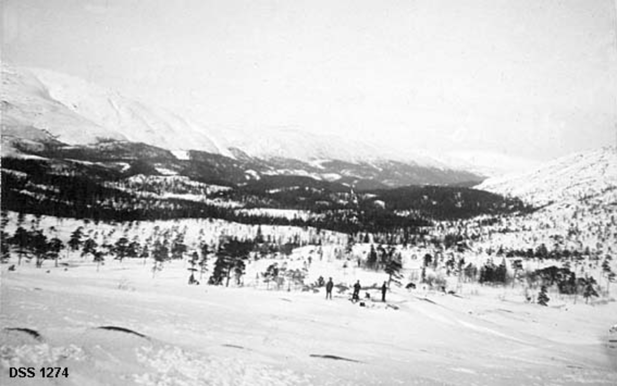 Eiterådal sett fra Ståvassheia.  Fotografiet er tatt fra ey høyt punkt ned mot en snødekt dal med en del barskog, omgitt av høye, trebare fjell.  På en rabbe i forgrunnen står tre mannlige skiløpere. 