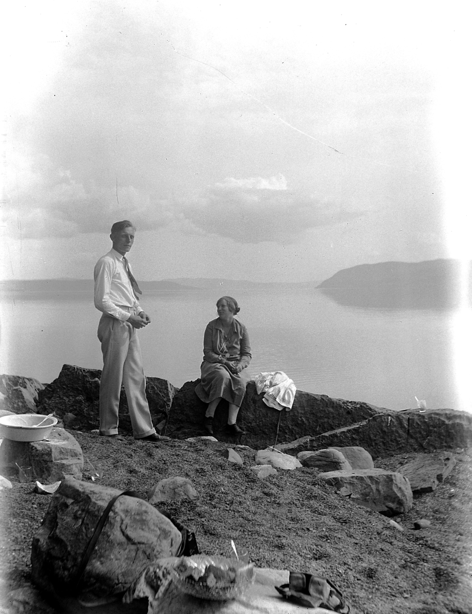 Mann og kvinne på stranda nedenfor Kvalstua, Helgøya. Skreia og Tangenodden i bakgrunnen.