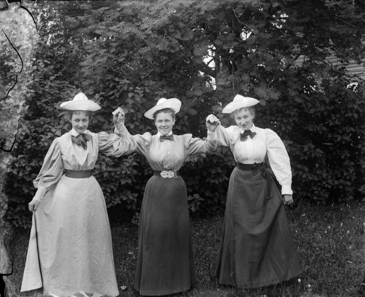 Tre kvinner med hatter holder hverandre i hendene i en hage. Lol Misen (f. Mellbye) t. v. 