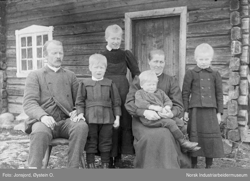 Familien Dillekås sittende utenfor laftet bygg i søre Kleive