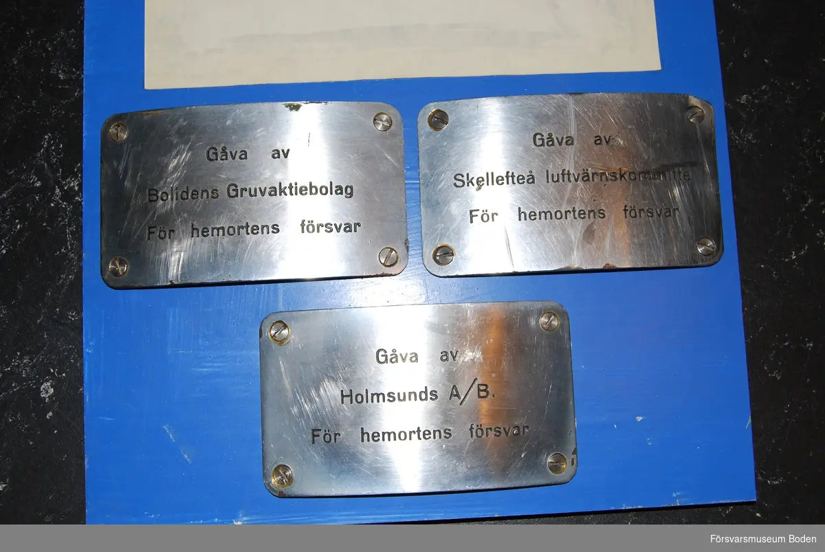 Gåvoskyltar för luftvärnspjäser som skänktes till försvaret under andra världskriget. Monterade på tavla under 1960-talet för utställning på gamla Garnisonsmuseet, Boden. Skyltarna kom från Bodens Tygstation. Gåvobrevet är daterat 6/9 1961.