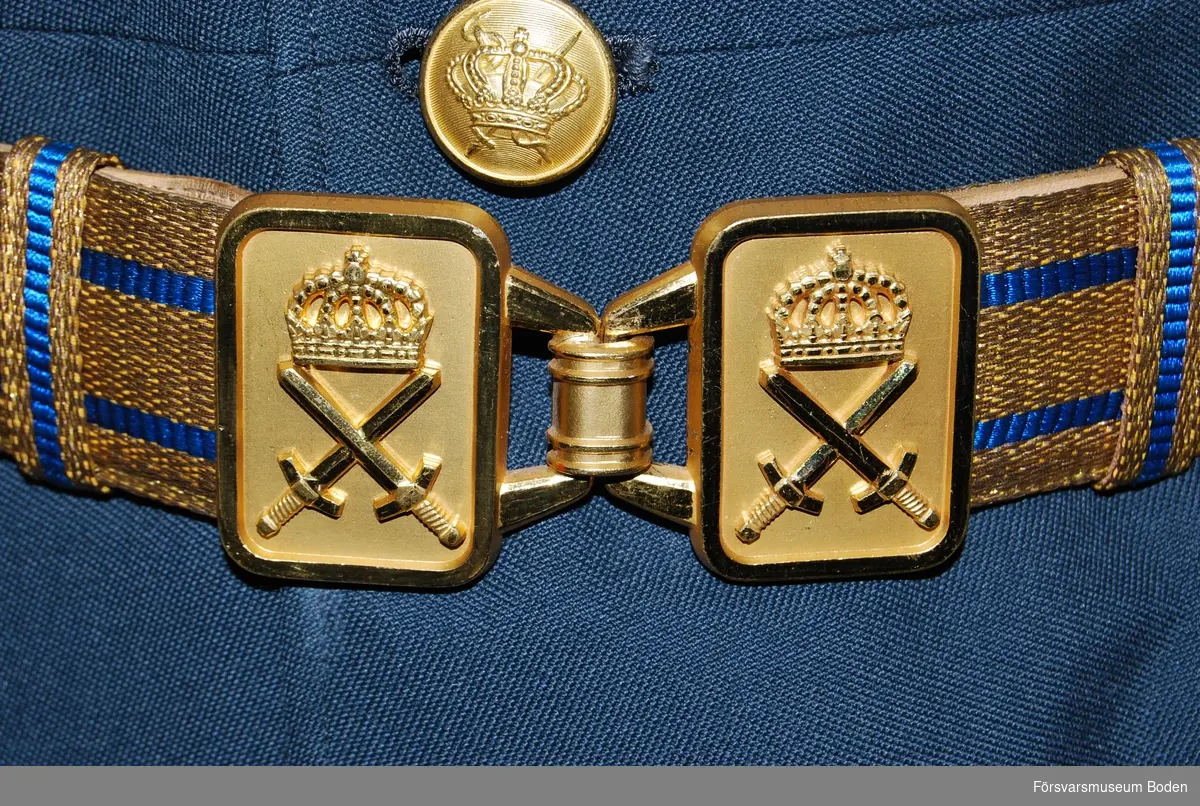 Guldfärgat silke med två blå ränder i centrum. Ljusbrunt skinn på baksidan. Spänne i guldfärgad metall med korslagda svärd under kunglig krona. Används till stor högtidsdräkt.