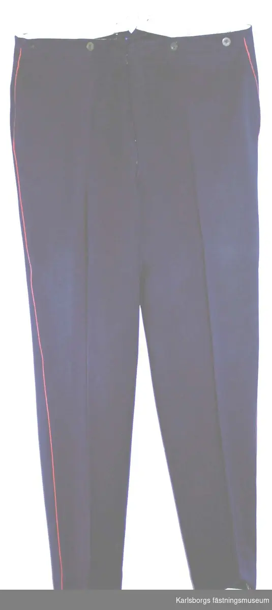 Långbyxa m/1886 i mörkblått kläde. Midjeband med knappar för hängslen . Gylf med knappar o hyska. En bakficka. På byxbenens sidsömmar rött fyrkantssnöre.
