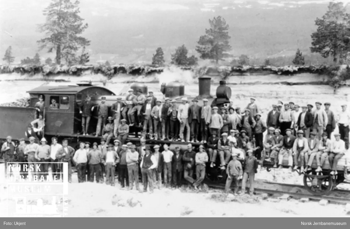 Rundt 80 mann oppstilt for fotografering på damplokomotiv nr. 236 og en grusvogn på Raumabaneanlegget
