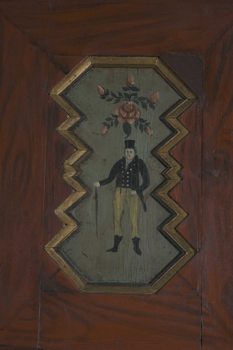 Doble dører oppe, to skyvedører på midten, en dør nede og to skuffer. Malte moriver: to adelsmenn og to blomster med nakne figurer oppi. Samson og løven på nedre skapdør. Marmorering i nisjen. Skyvedørene er dekorert med hester, kuer og geiter samt hus og en kirke.