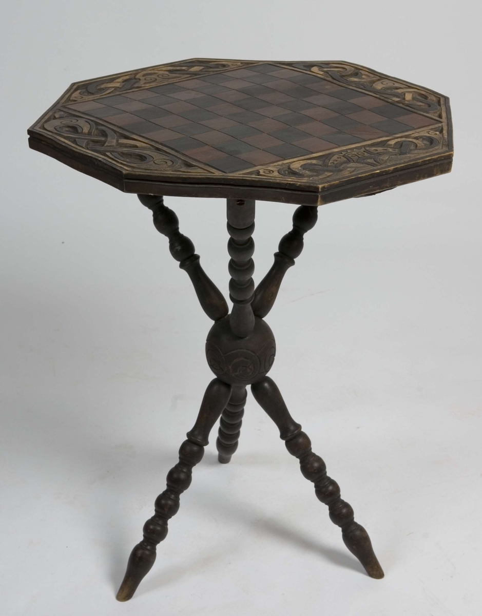 Åtte-kantet bordplate med sjakkrutemønster og skåret dekor på tre dreide bein.