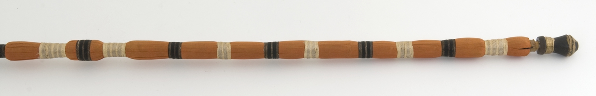 Lang, smal pipe i tre med hode og munnstykke i svart leire, dekormalt med gullfarge. Skaft kledd i tekstil i forskjellige farger.