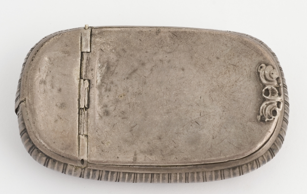 Dåse til finskåret skråtobakk, sølv, oval, buet, presset bladbord langs siden, stemplet innvendig i bunnen.