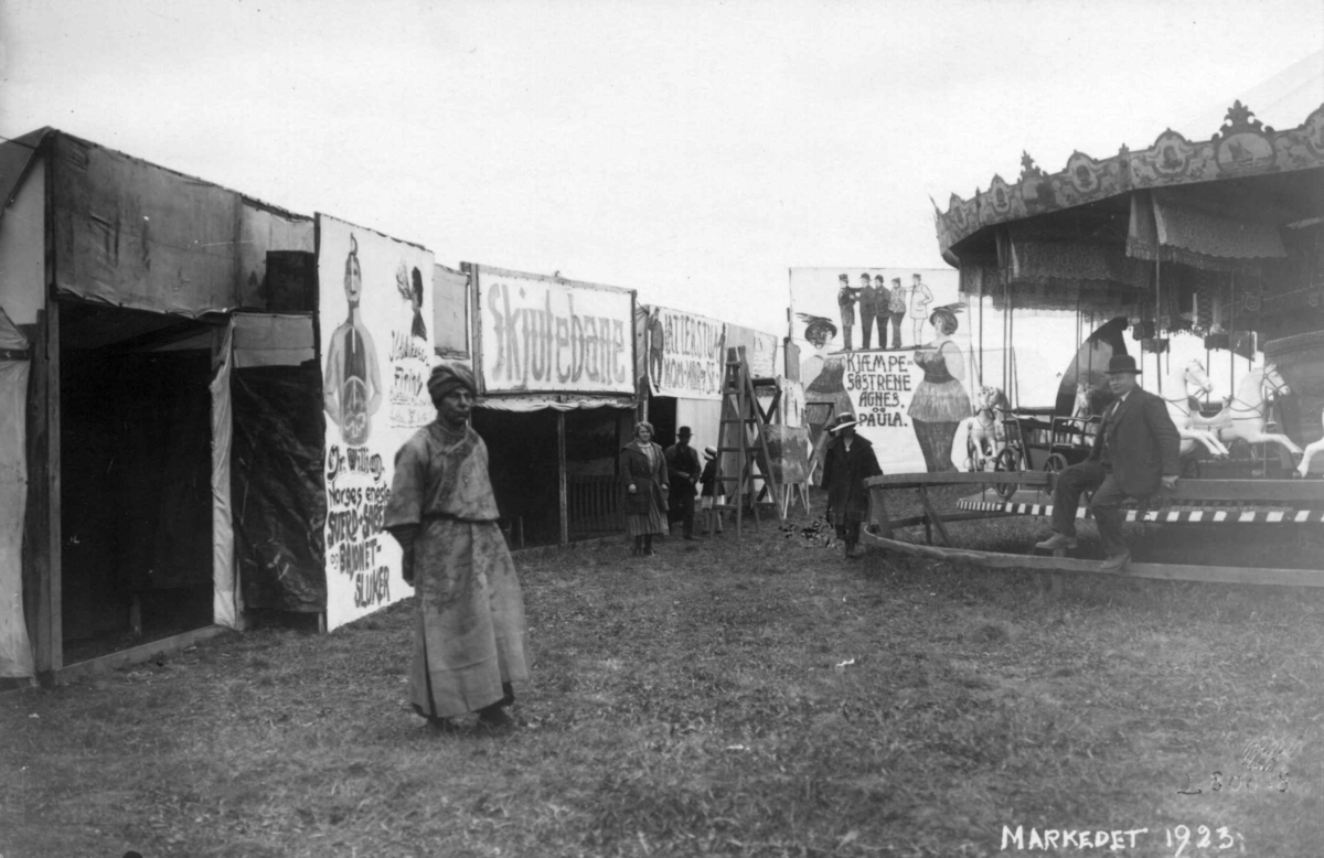 Marked på Norsk Folkemuseum i 1923. Karusell og boder som på et tivoli. Mann med turban.