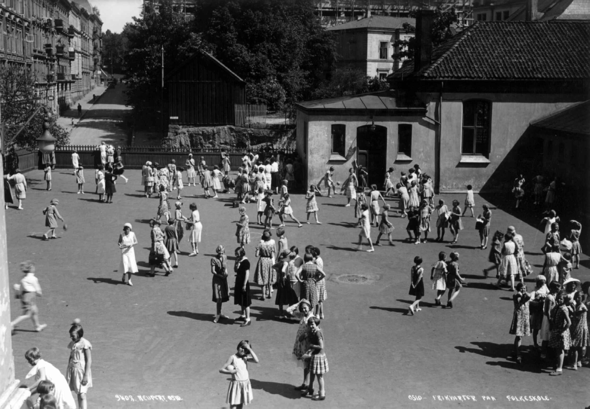 Ruseløkka skole, Oslo. 1932. Skolegård. Frikvarter. Skolebarn. Lærerinner. Bygate i bakgrunnen.