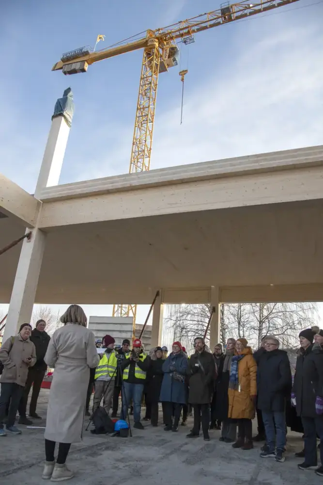 Deltakerne på grunnsteinsnedleggelsen står under tak, men over troner en byggekran som viser at dette er en travel byggeplass.