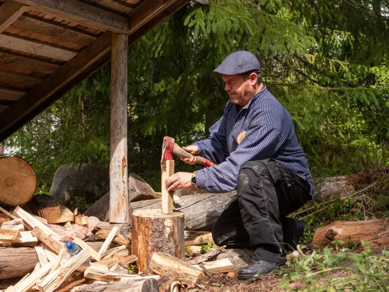 Mann sitter på kne og kløyver ved med en øks 