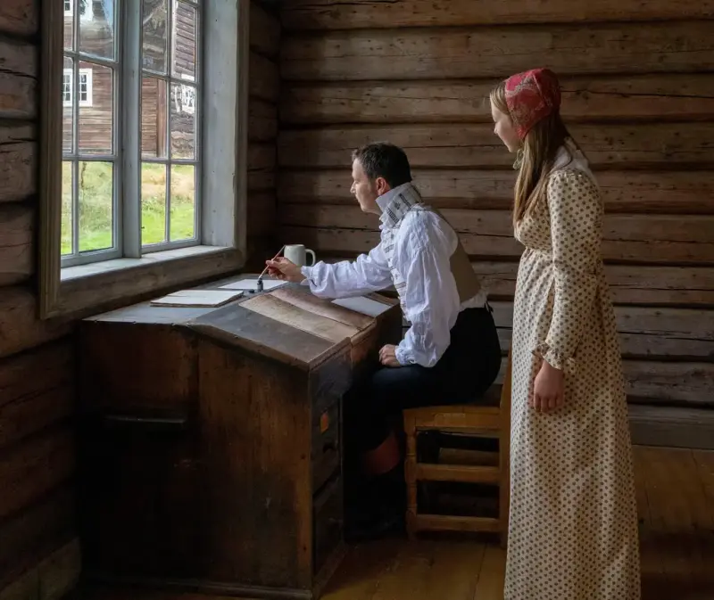 mann og kvinne kledd i gamle klær. Mannen skriver et brev med blekk 