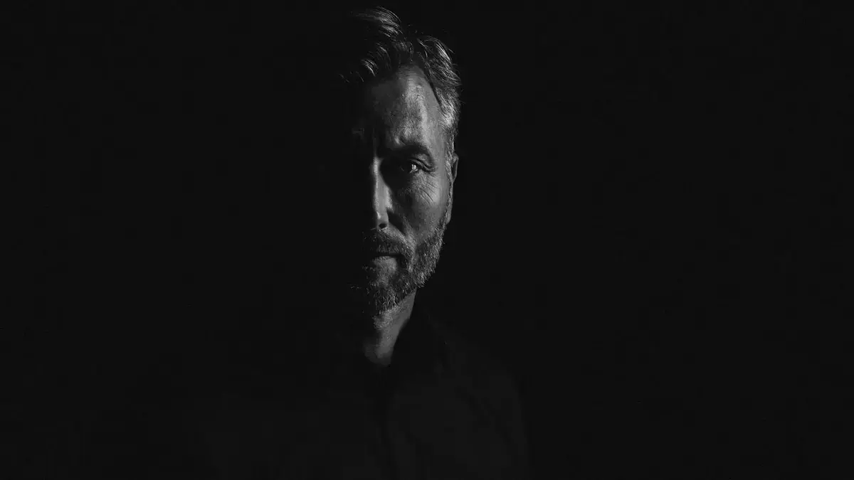 Portrettfoto av Helge Kaasin i eit mørkt rom der berre halve andlete synes