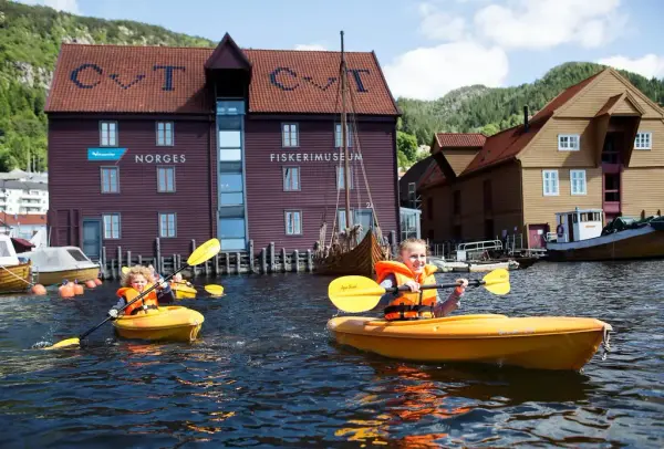 VI ser to barn som padler i hver sin gule kajakk i havnen foran Fiskerimuseet